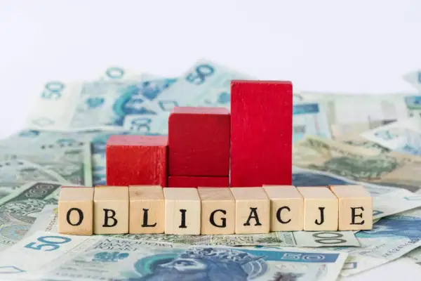 Drewniane klocki z napisem "OBLIGACJE" na tle polskich banknotów. Czy obligacje skarbowe są bezpieczne?