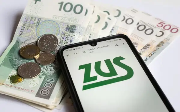 Złote banknoty i monety na nich leżący smartfon z logo ZUS.